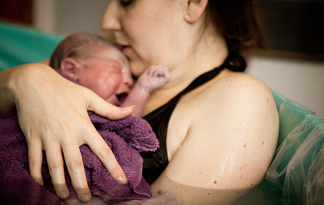 Picture of a woman in birth pool holding newborn.