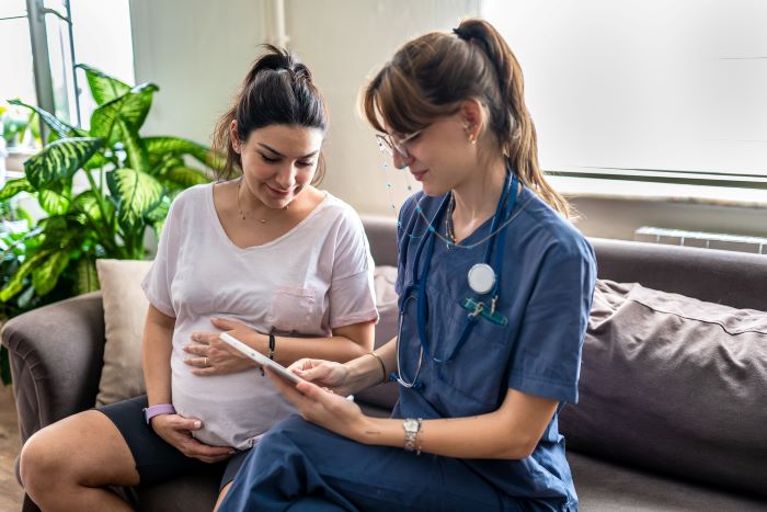 Health care provider visiting a pregnant client at home on the couch with an electronic tablet device.
