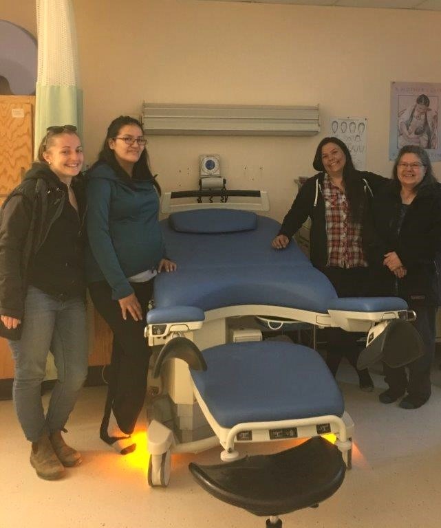 Care providers and expectant parent pose beside new birth bed.