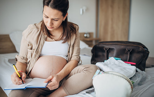 Photo of a pregnant person writing in a notebook.
