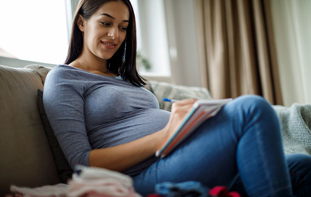 Photo of a pregnant person writing on a notepad.