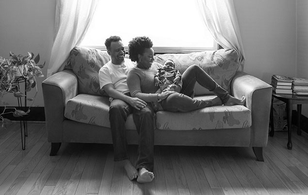 Photo of parents seated at home with newborn.