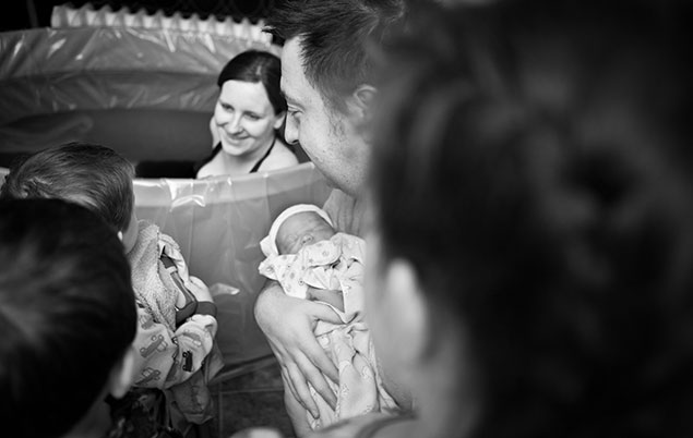 Picture of a woman in a birth pool surrounded  by 3 children and her partner who is holding their newborn.