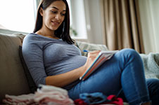 Photo of a pregnant person writing on a notepad.