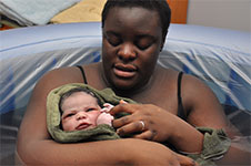 Photo of a birthing person holding a newborn in a birth pool.