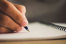 Photo of a hand making notes in a notebook.