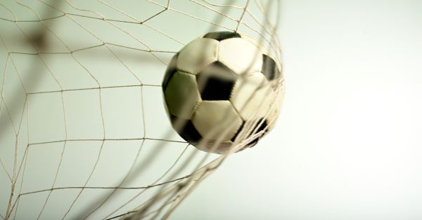 Soccer ball in net with grey sky backdrop.