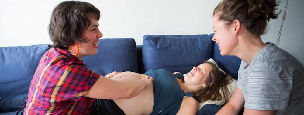 Midwife performs belly check on a client while her partner looks on