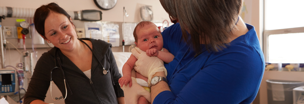 Physician looks on as midwife holds baby