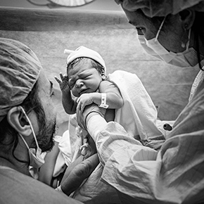 Newborn being held by midwife and father