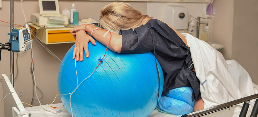 Picture of laboring woman leaning over a birth ball in hospital bed.