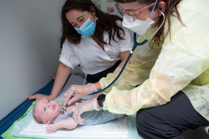 Midwife performs well-baby visit at a postpartum clinic appointment while mother observes.