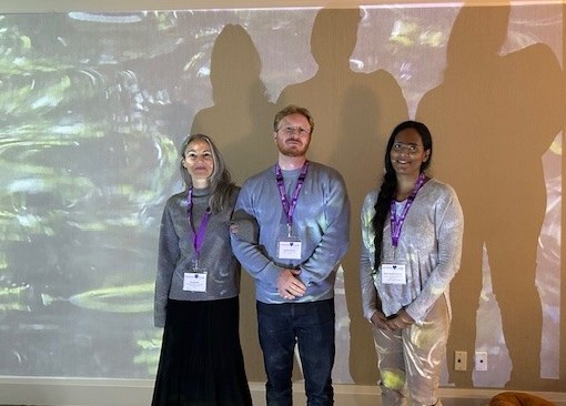 Three presenters standing in front of projected virtual backdrop.