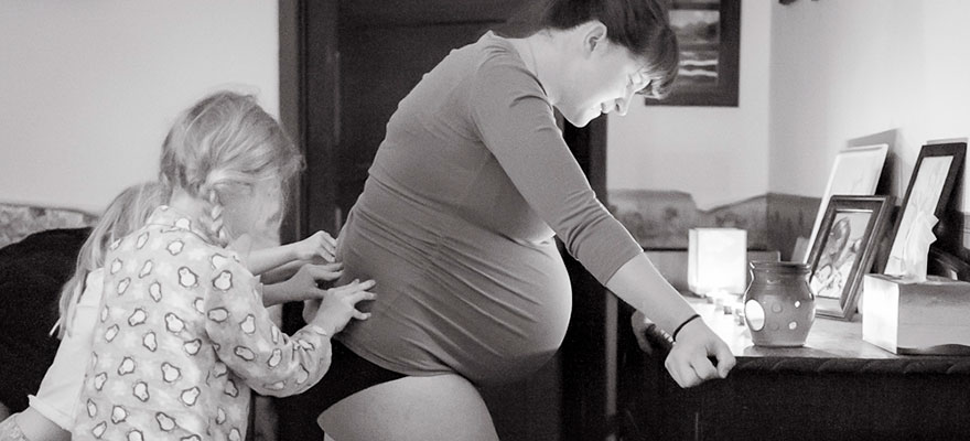 Picture of two children massaging labouring woman’s back while she leans onto a table.