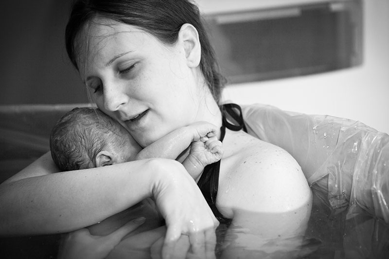 Picture of a woman in birth pool holding newborn baby up their cheek.