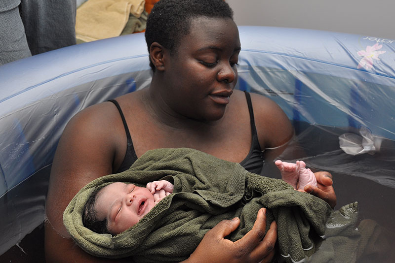 Picture of a woman in birth pool holding their newborn wrapped in a towel.